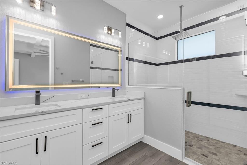 Full bathroom with a shower stall, double vanity, light wood-style floors, and recessed lighting