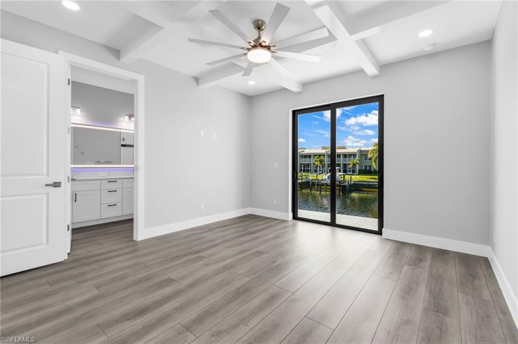 Empty room with a water view, coffered ceiling, beam ceiling, light wood finished floors, and recessed lighting