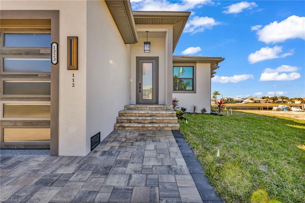 Doorway to property with stucco siding and a lawn