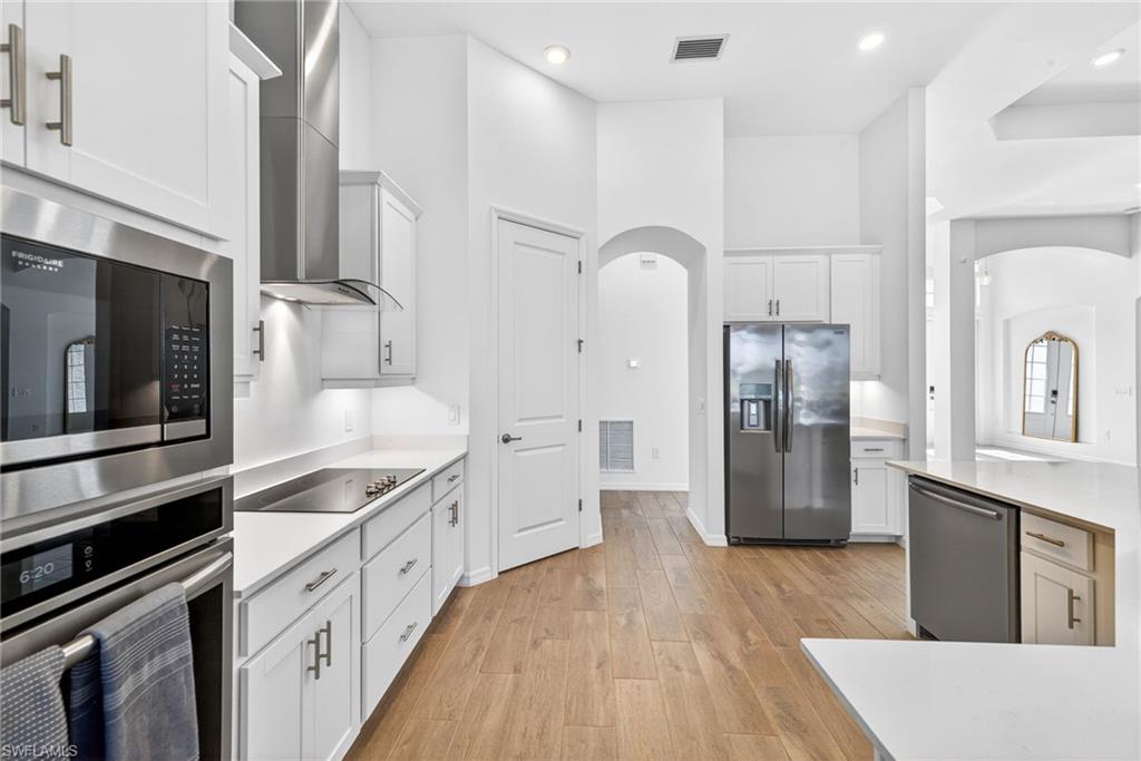 Kitchen with appliances with stainless steel finishes, white cabinets, wall chimney exhaust hood, light wood-style flooring, and a high ceiling