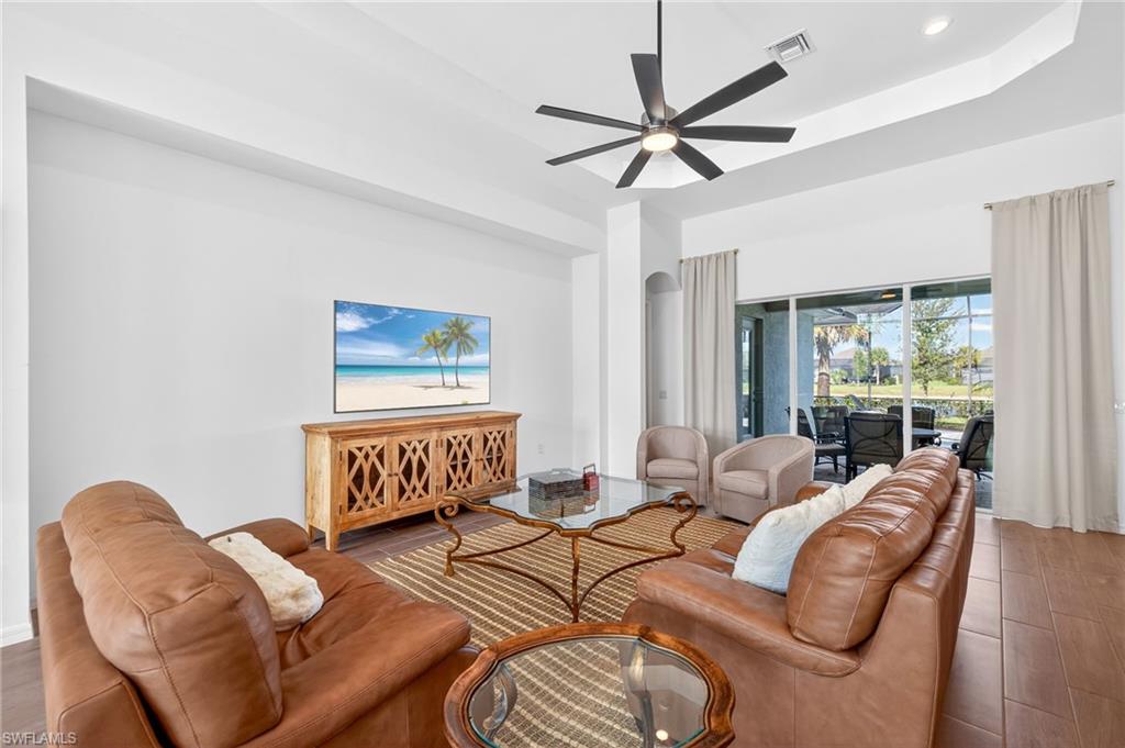 Living room featuring a tray ceiling, a ceiling fan, wood finished floors, and recessed lighting
