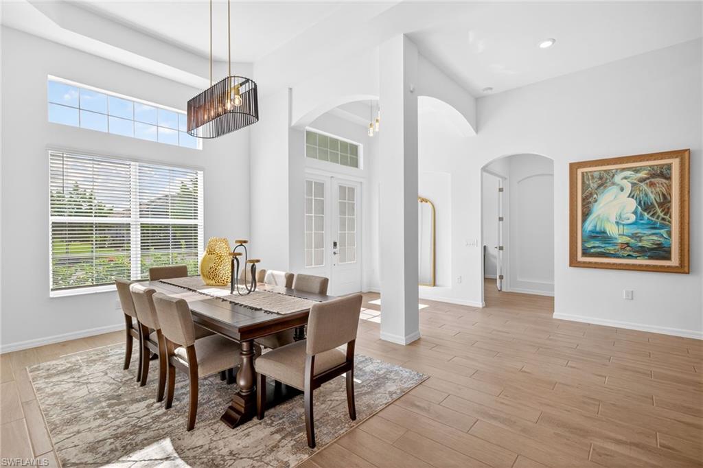 Dining area featuring arched walkways, french doors, light wood finished floors, and a towering ceiling