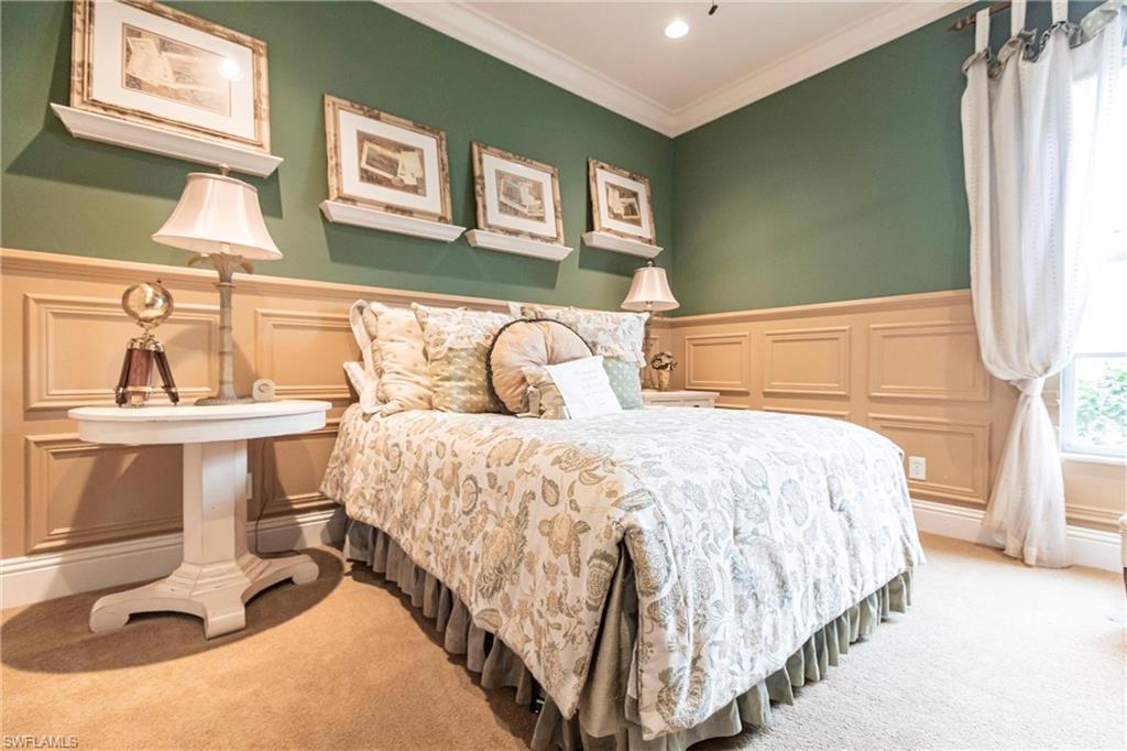 Bedroom featuring carpet flooring, crown molding, wainscoting, and a decorative wall