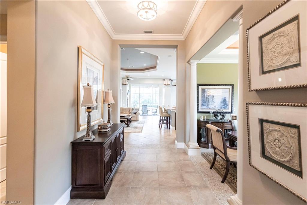 Hall with ornate columns, a tray ceiling, crown molding, and light tile patterned flooring