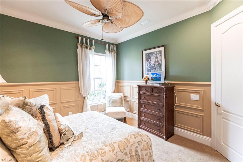 Bedroom with wainscoting, a decorative wall, crown molding, carpet flooring, and a ceiling fan