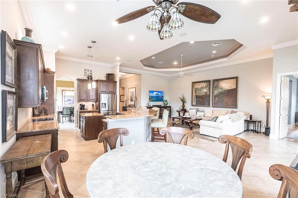 Dining space featuring crown molding, arched walkways, a ceiling fan, a tray ceiling, and light tile patterned floors