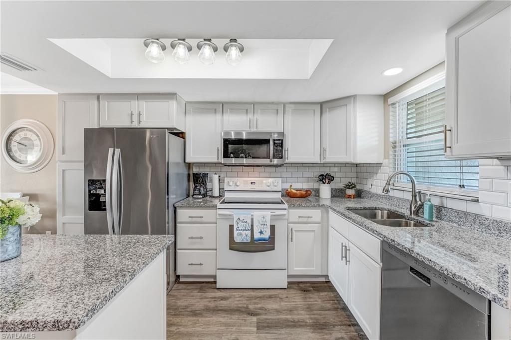The kitchen offers white shaker-style cabinetry, stainless steel appliances, a center island, granite countertops, new lighting, and a classic subway tile backsplash.