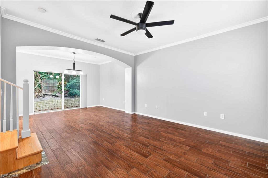 Unfurnished living room with crown molding, dark wood-type flooring, ceiling fan, stairs, and arched walkways