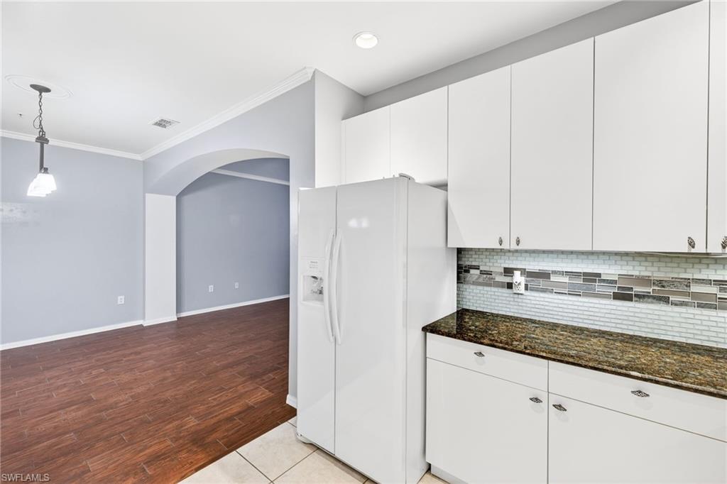Kitchen with dark stone countertops, ornamental molding, white cabinetry, white refrigerator with ice dispenser, and arched walkways