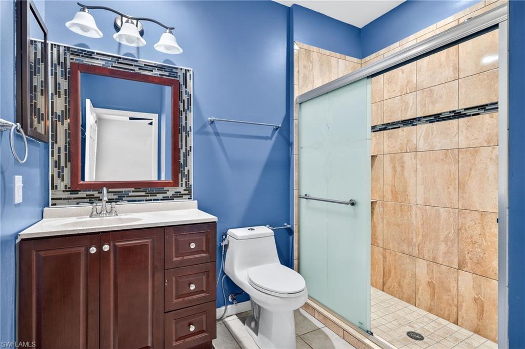 Bathroom featuring a stall shower, vanity, backsplash, and light tile patterned floors