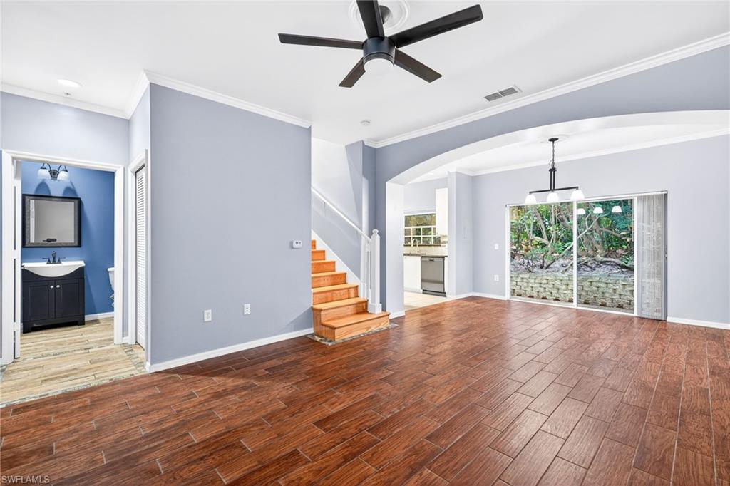 Unfurnished living room featuring wood finish floors, ornamental molding, stairs, ceiling fan, and arched walkways