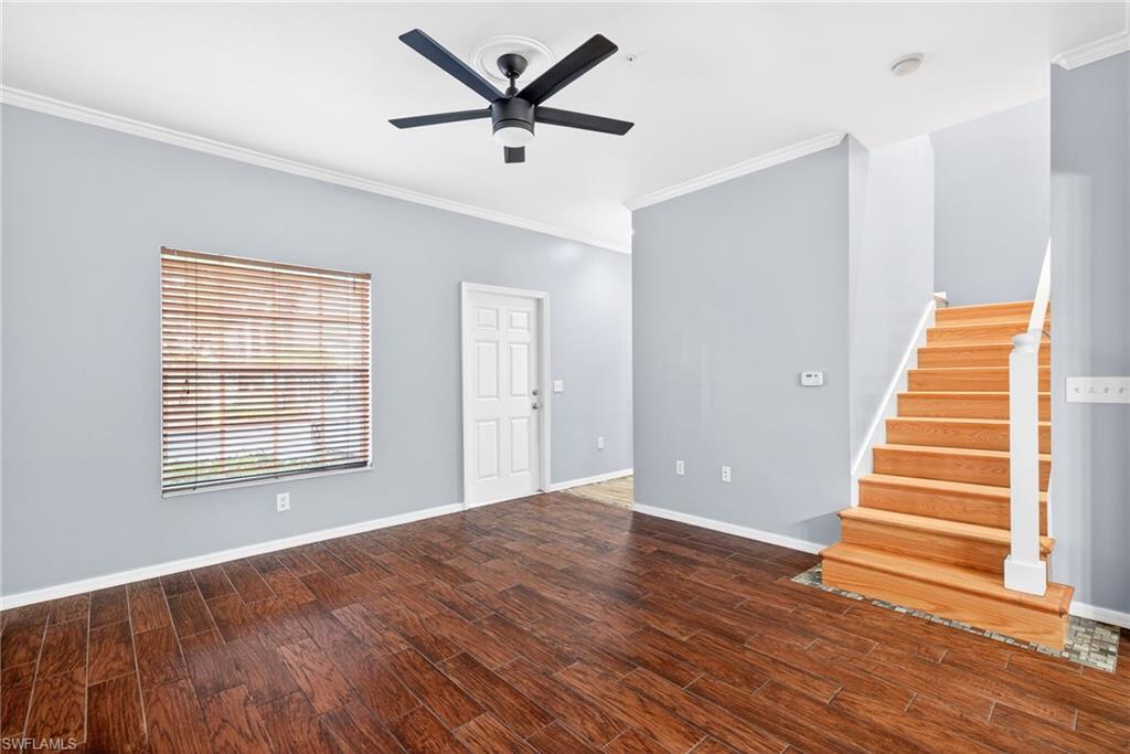 Unfurnished living room with crown molding, stairway, dark wood finished floors, and a ceiling fan
