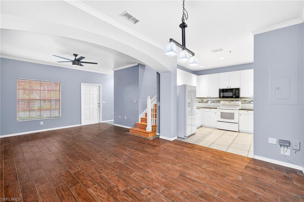 Unfurnished living room featuring arched walkways, ceiling fan, electric panel, crown molding, and stairway