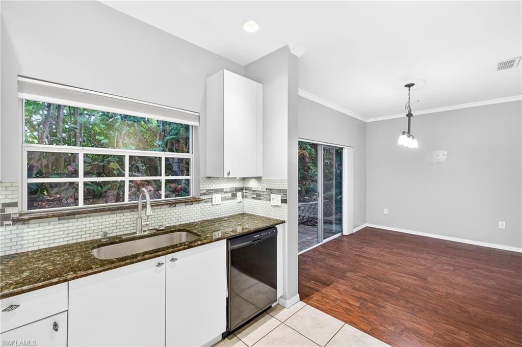 Kitchen with dark stone counters, backsplash, dark tile patterned flooring, dishwasher, and decorative light fixtures