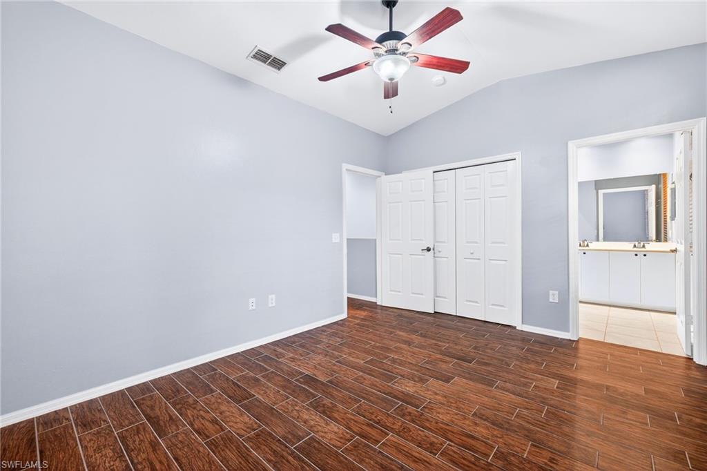 Unfurnished bedroom with lofted ceiling, wood finish floors, a closet, ceiling fan, and ensuite bathroom