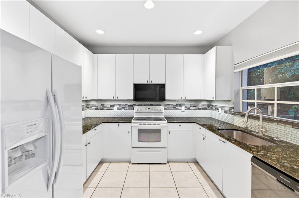 Kitchen featuring white appliances, dark stone counters, white cabinets, decorative backsplash, and recessed lighting