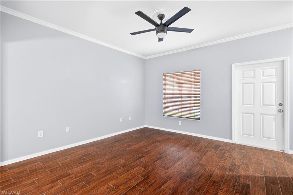 Empty room featuring crown molding, dark wood-style floors, and ceiling fan