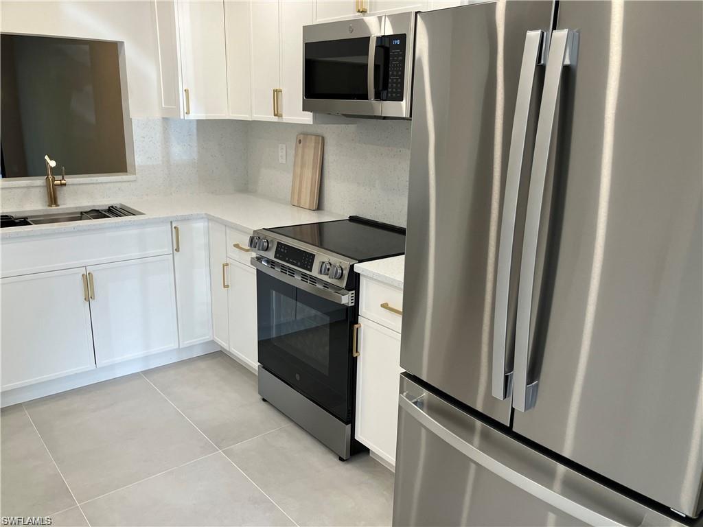Kitchen featuring stainless steel appliances, decorative backsplash, light tile patterned floors, white cabinetry, and light stone countertops