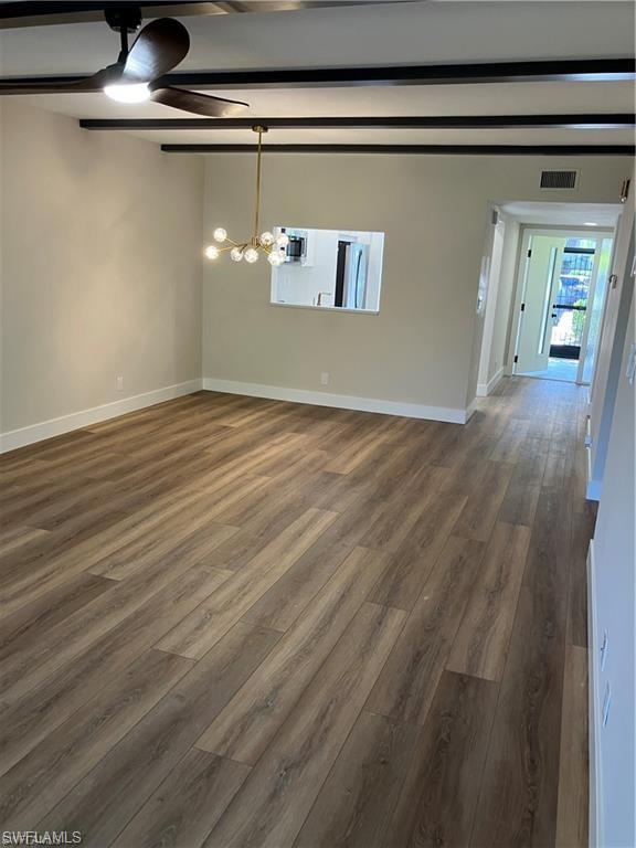 Unfurnished dining area with dark wood-style flooring, a ceiling fan, beam ceiling, and a chandelier