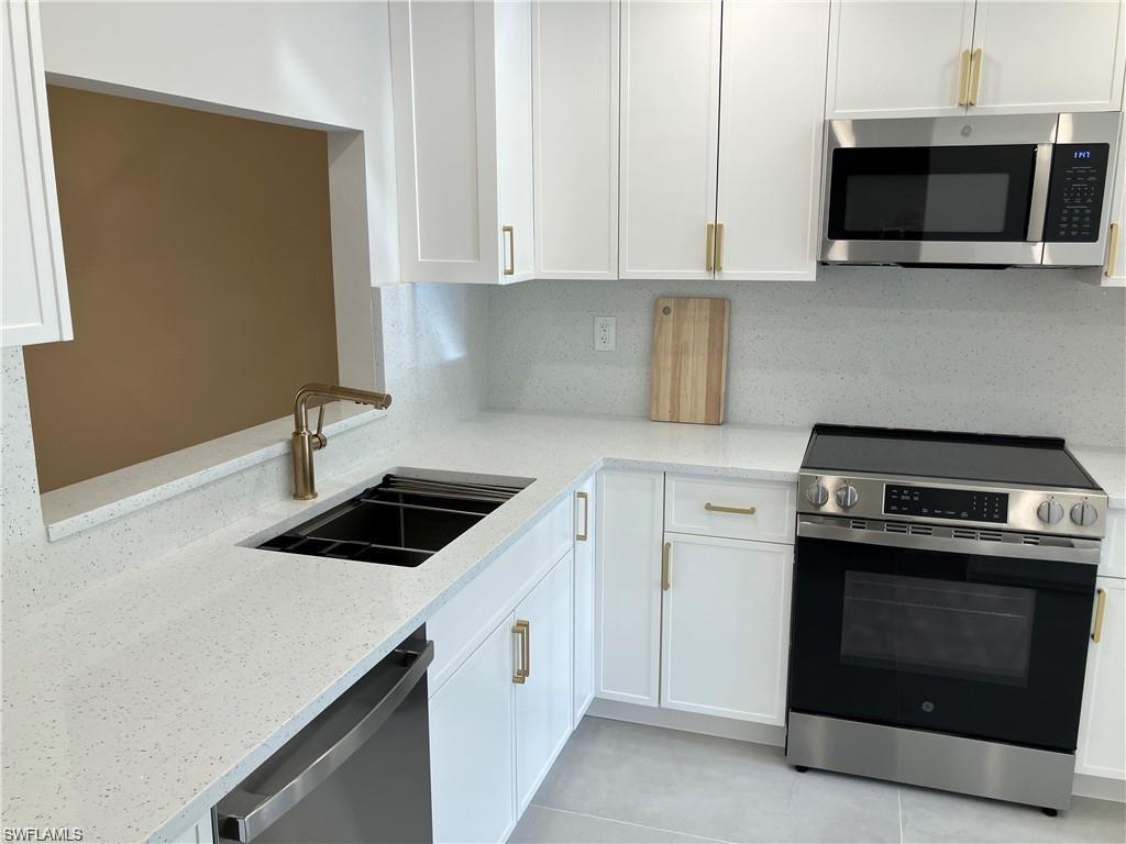 Kitchen with stainless steel appliances, white cabinetry, light stone countertops, and backsplash