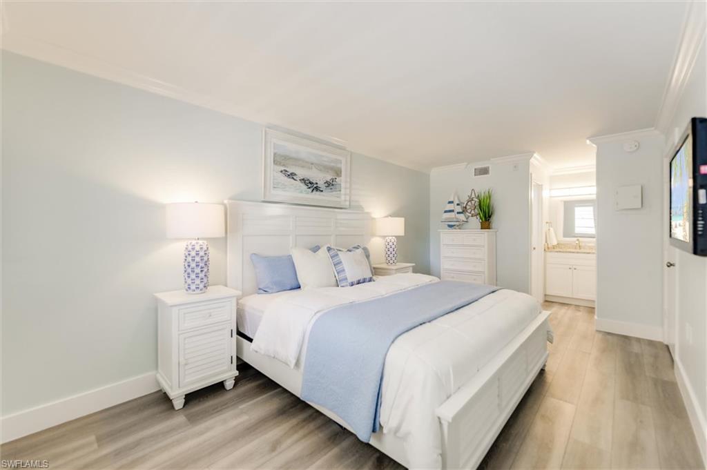 Bedroom with light wood-style flooring, ornamental molding, and connected bathroom
