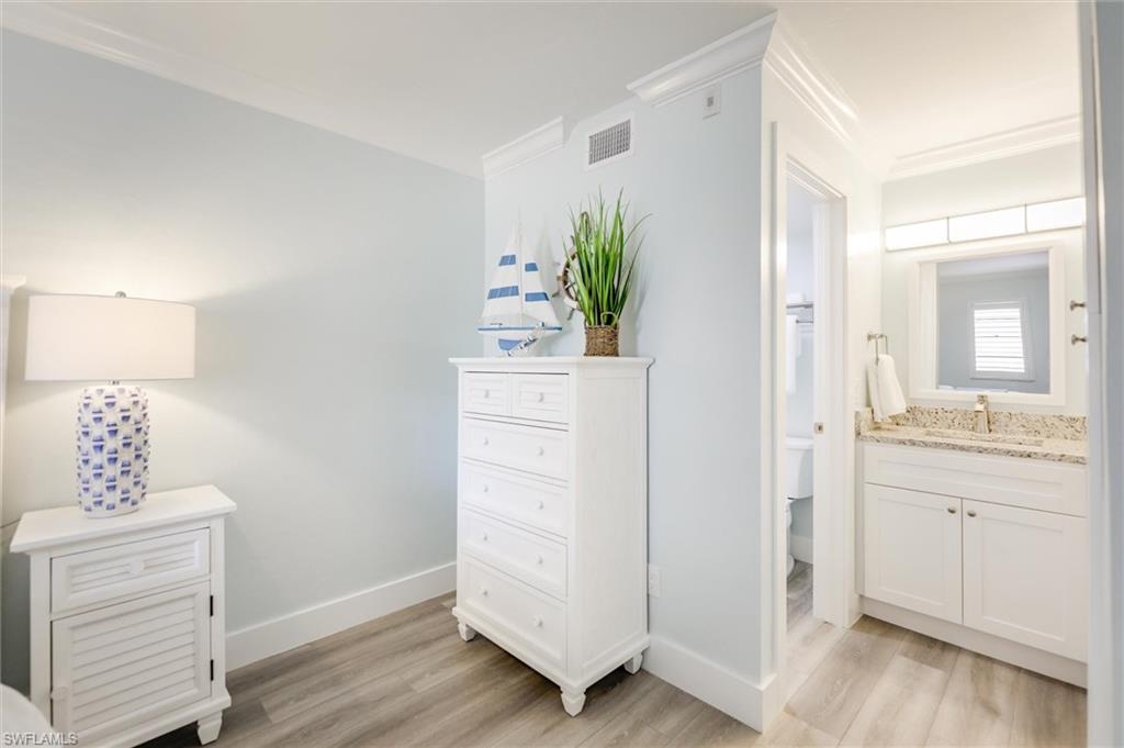 Bedroom featuring light wood finished floors, ornamental molding, and connected bathroom