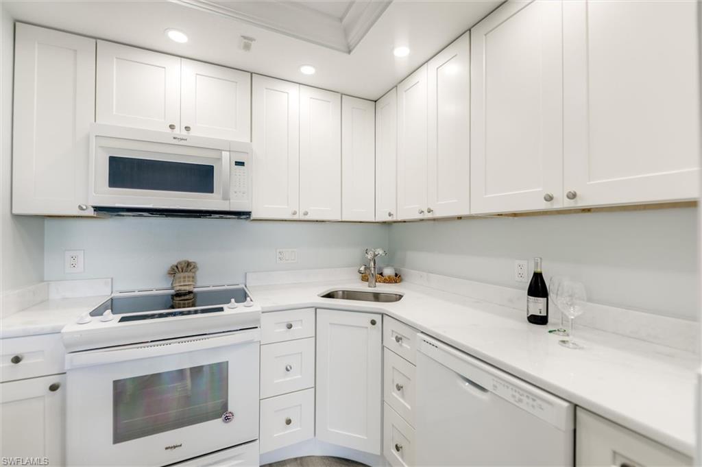Kitchen with white appliances, white cabinets, recessed lighting, light stone countertops, and ornamental molding
