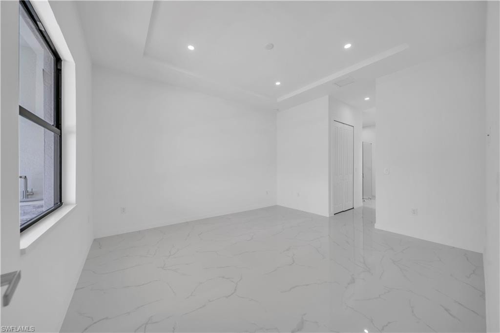 Spare room featuring recessed lighting, a raised ceiling, and light marble finish flooring