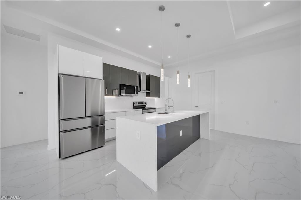 Kitchen with stainless steel appliances, a center island with sink, hanging light fixtures, light stone counters, and white cabinetry