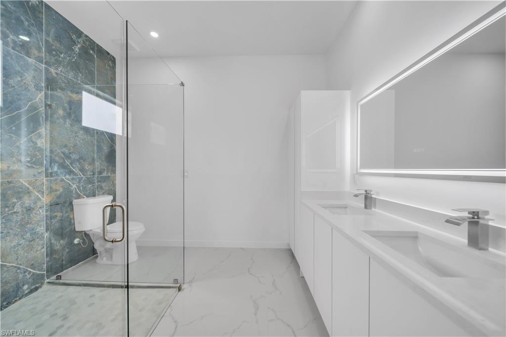 Bathroom featuring light marble finish flooring, double vanity, a stall shower, and recessed lighting