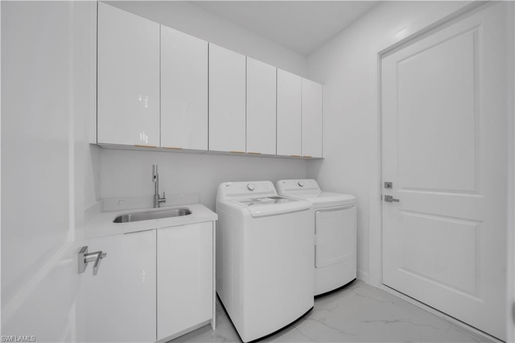 Laundry area featuring cabinet space, light marble finish floors, and washing machine and clothes dryer