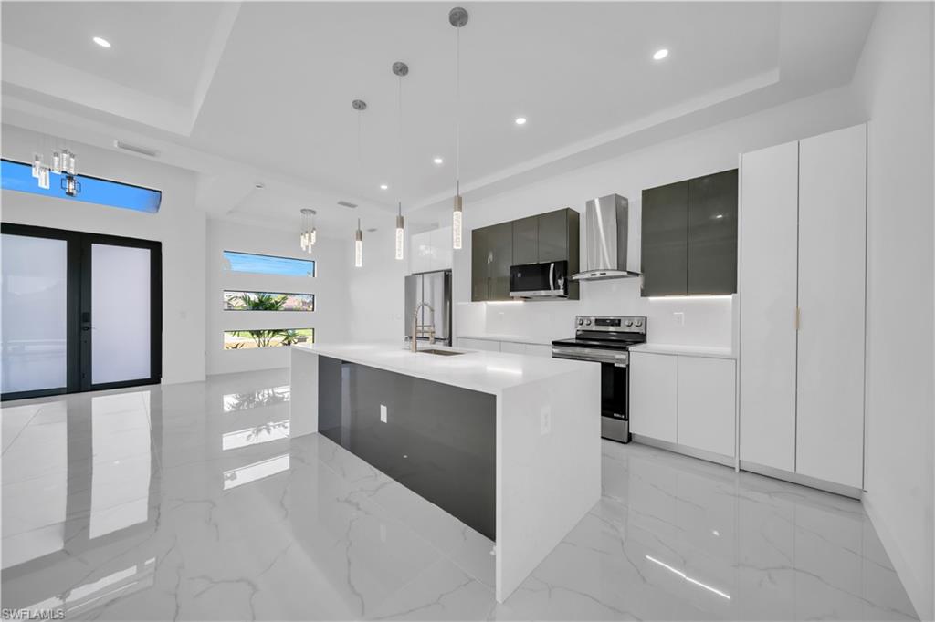Kitchen featuring stainless steel appliances, modern cabinets, light marble finish flooring, and a raised ceiling