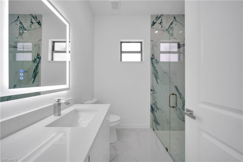 Bathroom with plenty of natural light, a marble finish shower, vanity, and light marble finish flooring