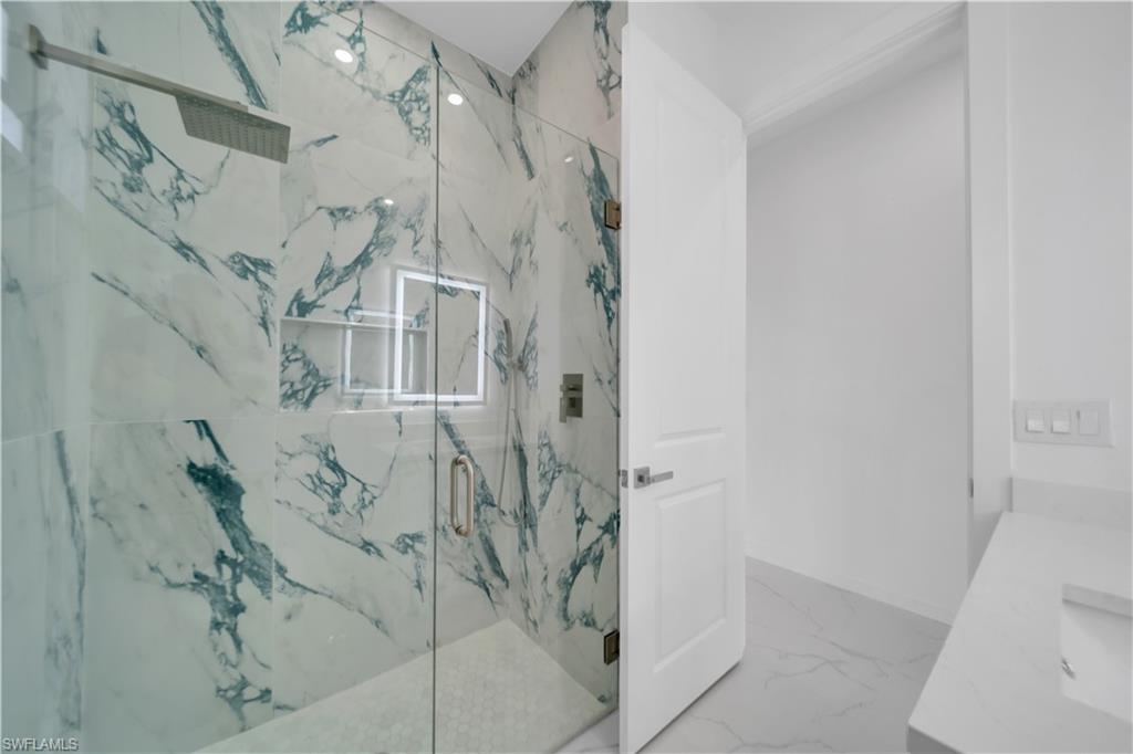 Bathroom featuring vanity, a marble finish shower, and light marble finish floors