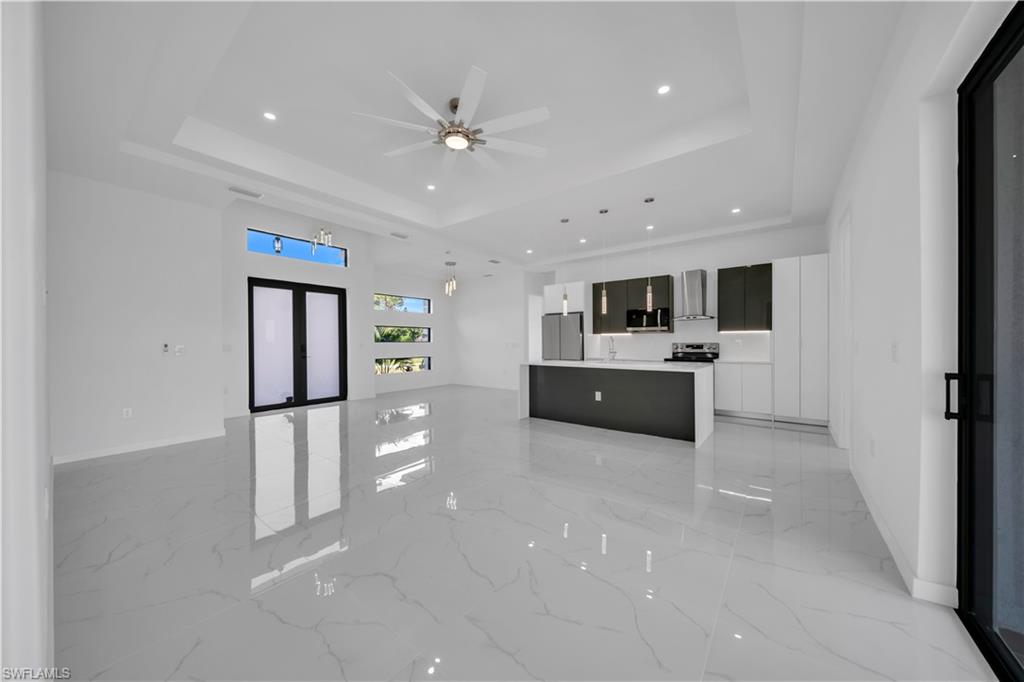 Unfurnished living room with light marble finish flooring, ceiling fan, recessed lighting, french doors, and a raised ceiling