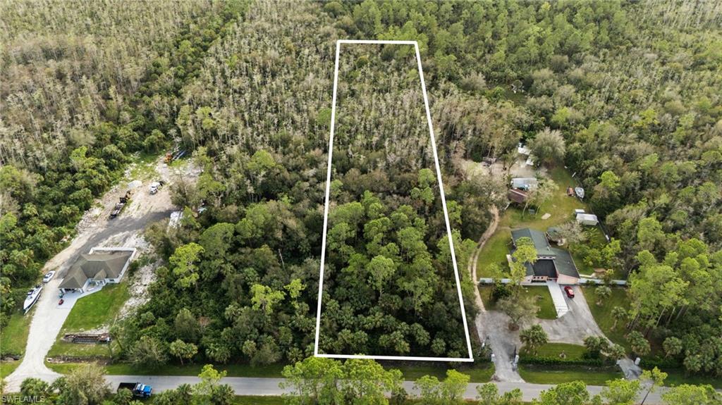 Aerial view of property and surrounding area with property parcel outlined and a forest