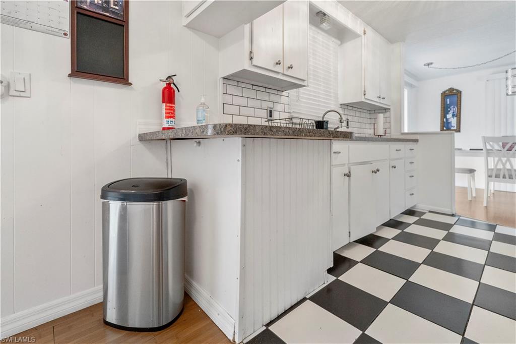 Kitchen with white cabinetry, light flooring, decorative backsplash, and dark countertops