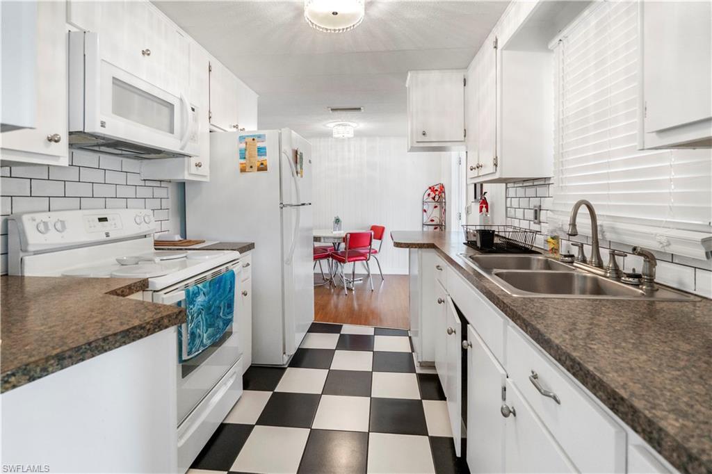 Kitchen with dark flooring, white appliances, decorative backsplash, and dark countertops
