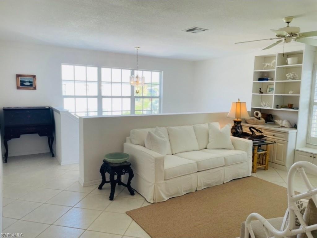 Living room featuring light tile patterned flooring, ceiling fan, and suspended lighting