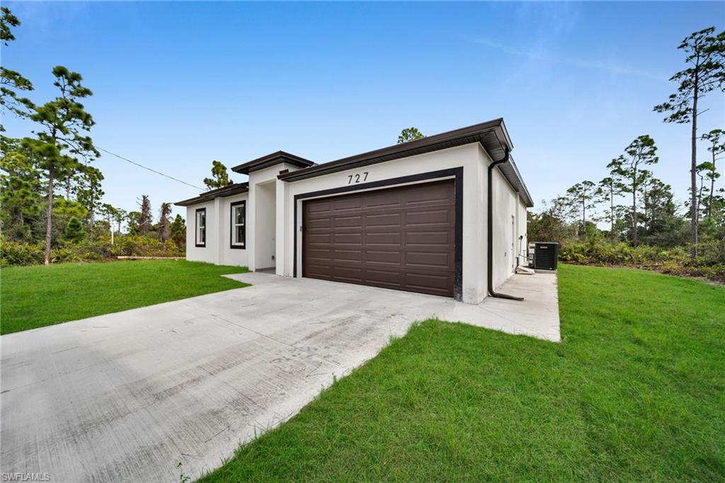 View of front facade with stucco siding, driveway, a front lawn, and an attached garage