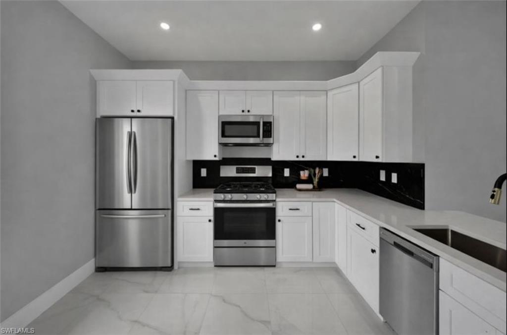 Kitchen featuring appliances with stainless steel finishes, white cabinets, backsplash, and light marble finish flooring