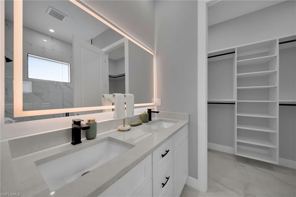 Bathroom with a walk in closet, light marble finish flooring, double vanity, a marble finish shower, and recessed lighting