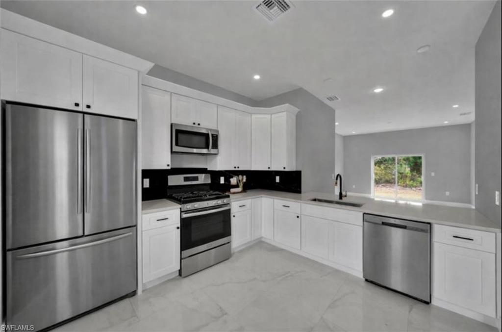 Kitchen featuring appliances with stainless steel finishes, white cabinetry, light marble finish flooring, recessed lighting, and light stone counters