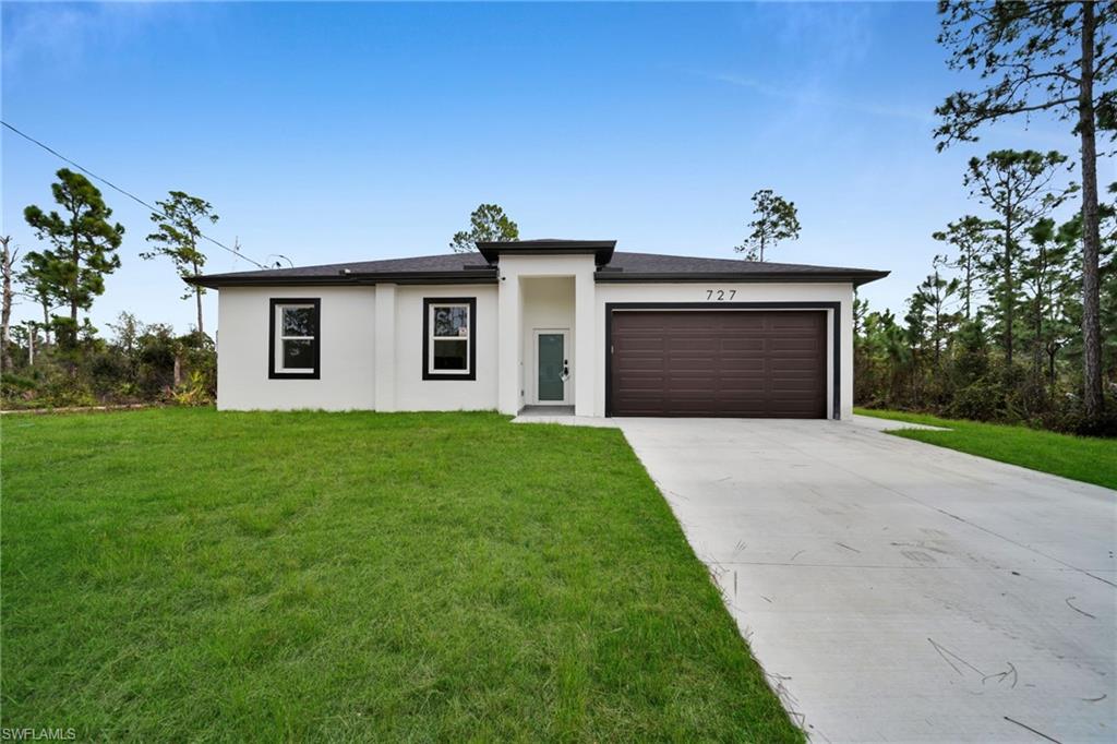 Prairie-style house with concrete driveway, a front lawn, stucco siding, and an attached garage