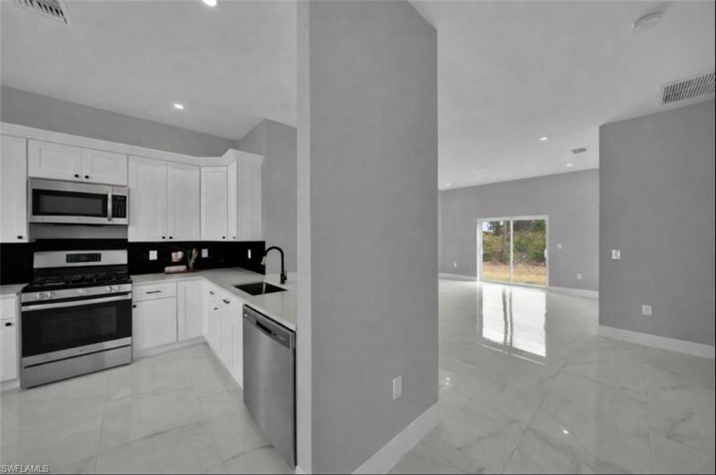 Kitchen featuring appliances with stainless steel finishes, light marble finish floors, white cabinets, backsplash, and recessed lighting