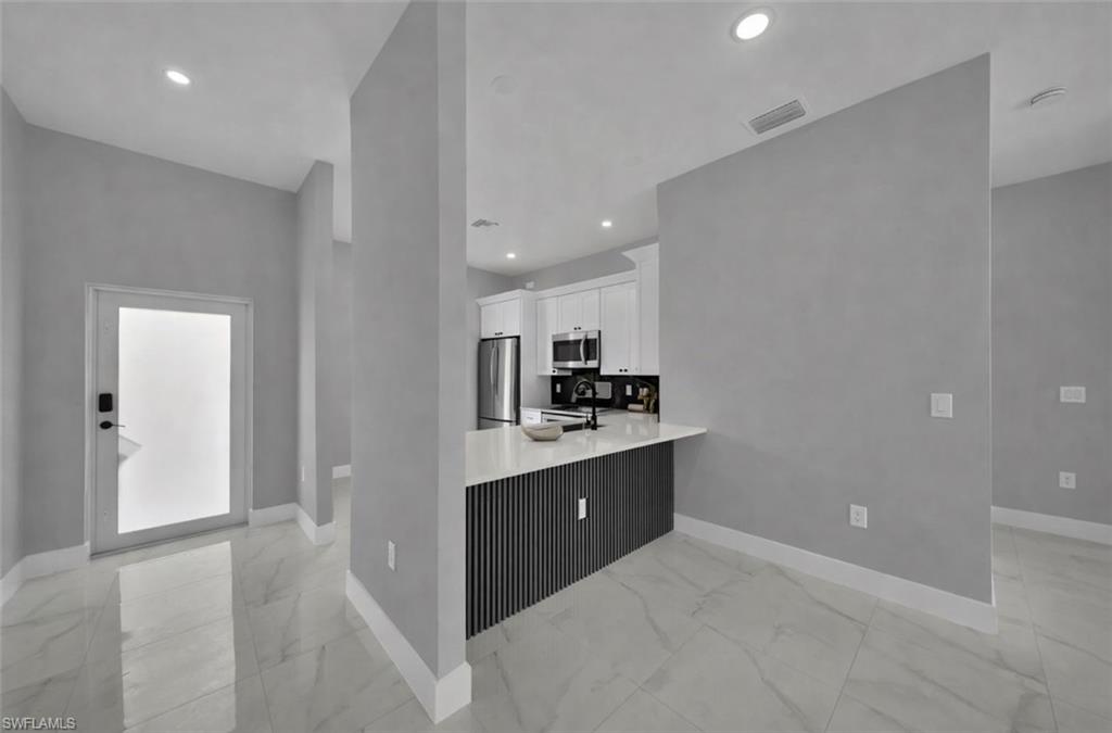 Kitchen with a peninsula, white cabinetry, appliances with stainless steel finishes, light marble finish flooring, and recessed lighting