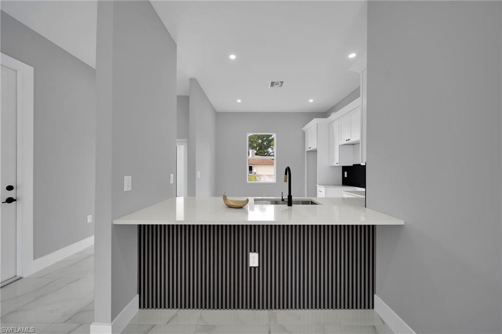Kitchen with white cabinetry, a peninsula, light marble finish floors, light stone countertops, and recessed lighting