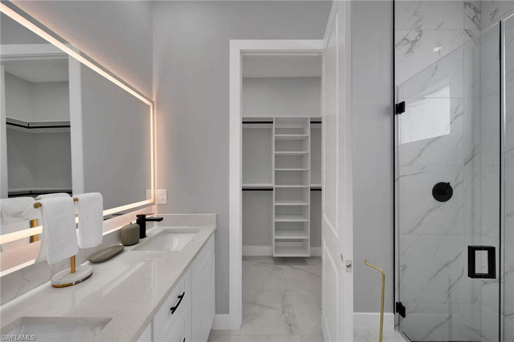 Bathroom featuring a walk in closet, double vanity, a marble finish shower, and light marble finish flooring