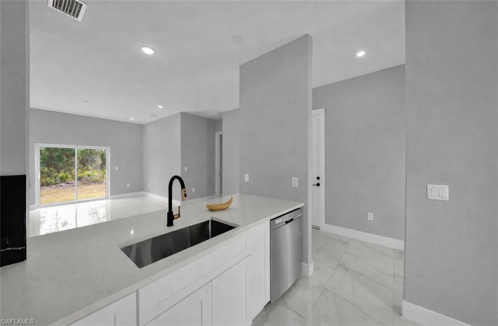 Kitchen with white cabinets, stainless steel dishwasher, light stone countertops, recessed lighting, and light marble finish floors
