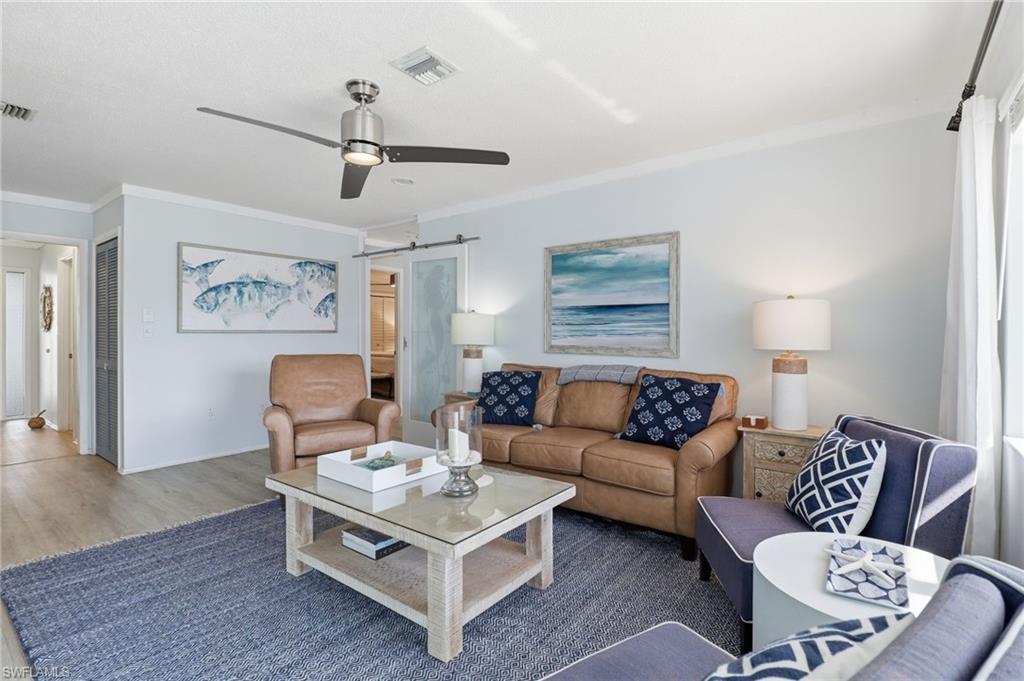 Living room featuring a barn door, ornamental molding, ceiling fan, and wood finished floors